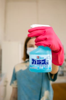 Person holding cleaning spray with gloves, emphasizing safety and hygiene.