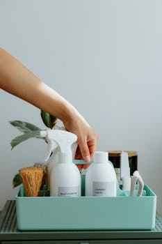 Hand arranging cleaning products in a tidy organizer, promoting cleanliness and order.