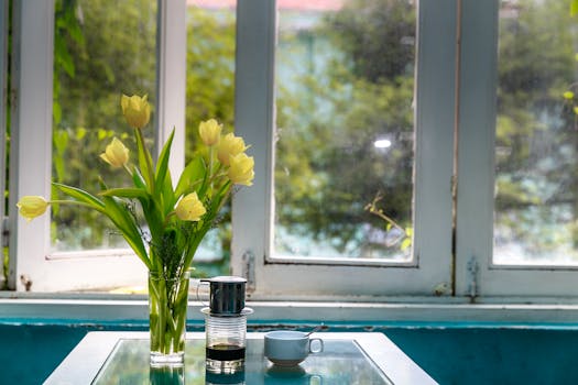 Bright indoor setting with yellow tulips in a vase and coffee on a glass table by a window.