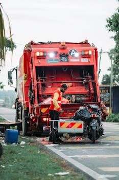 A sanitation worker managing waste disposal behind a garbage truck in Klang, Selangor.