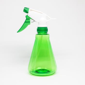 Close-up of a green plastic spray bottle on a white surface, ideal for cleaning products.
