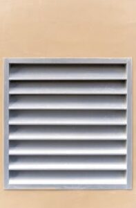 A minimalist exterior shot of a metal air vent against a beige wall, showcasing modern simplicity.