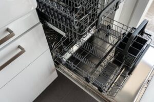 A clean and empty stainless steel dishwasher open in a modern kitchen setting.