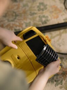 A person is changing the filter of a yellow vacuum cleaner indoors, showing a close-up view.