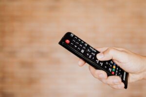 Close-up shot of a hand holding a TV remote control against a blurred background.
