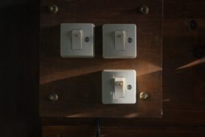 Close-up view of vintage light switches mounted on a wooden panel, illuminated softly in a dark interior setting.