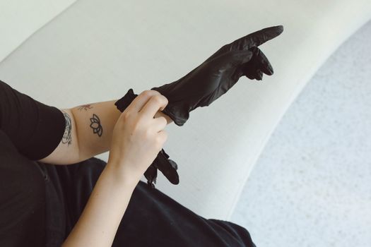 A person with a tattoo puts on black latex gloves, focusing on hand safety.